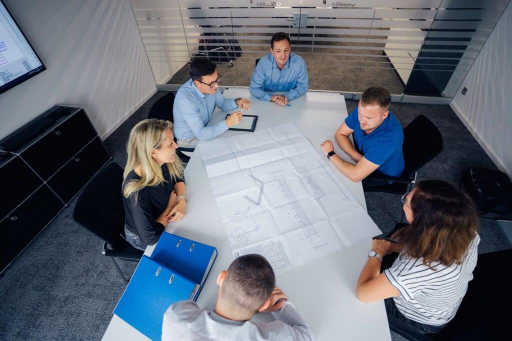 Mitarbeitende von Giesers Stahlbau GmbH in einem Konferenzraum mit Bauplänen