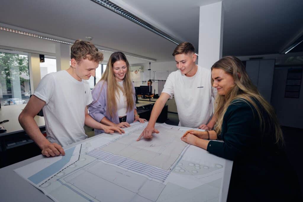 Junge Mitarbeitende von Giesers Stahlbau GmbH rund um einen Bauplan an einem Tisch