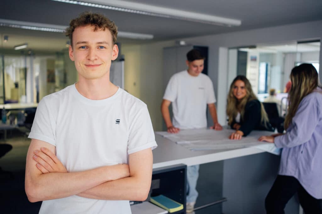 Mitarbeiter von Giesers Stahlbau GmbH mit verschränkten Armen und weiteren Mitarbeitern im Hintergrund versammelt um einen Bauplan