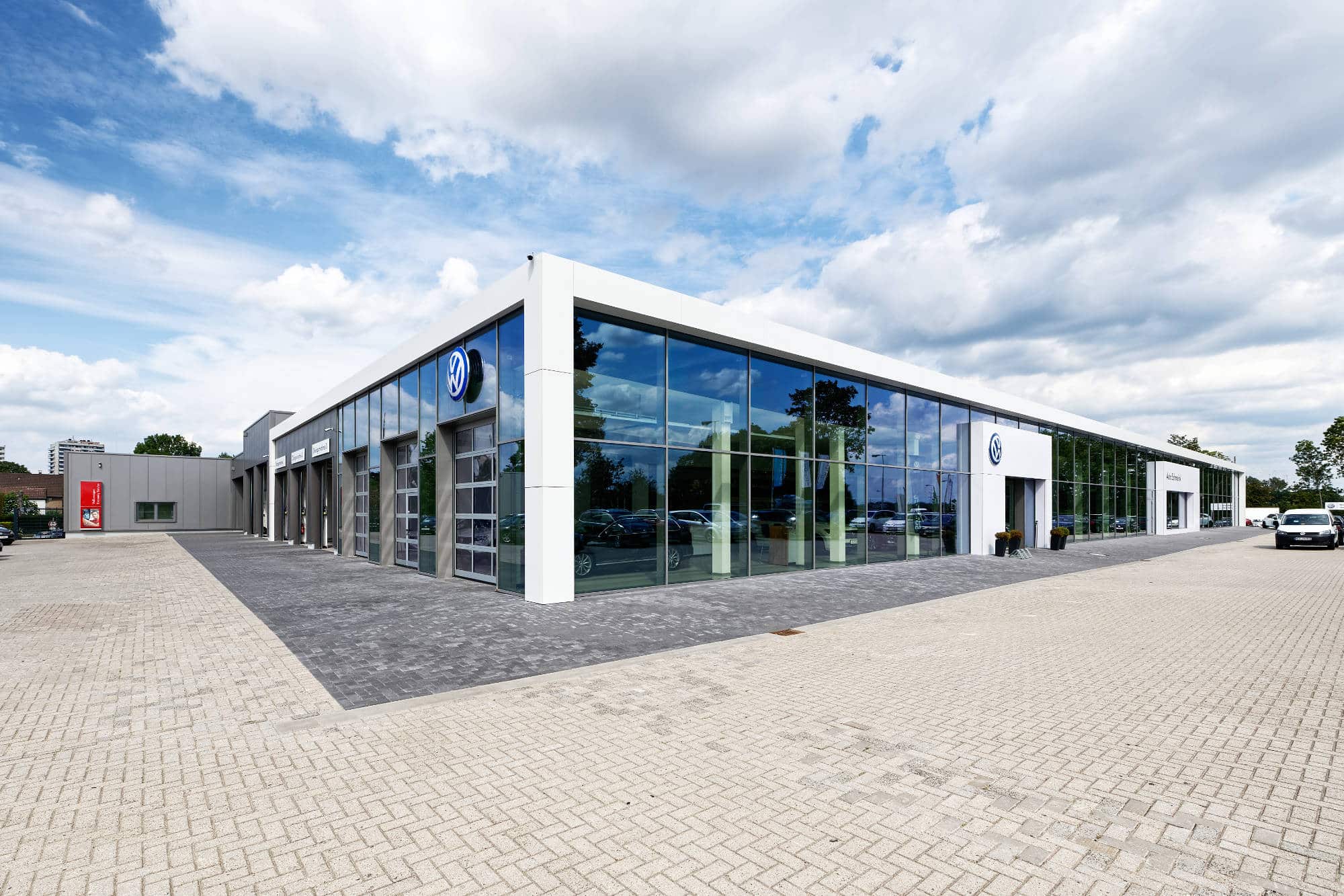 Außenansicht des fertiggestellten VW Autohauses Schmeink in Wesel mit verglaster Fassade und Werkstattzufahrt.